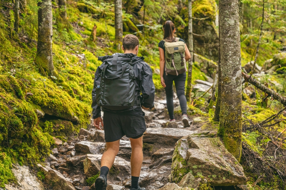 A man and woman hike in the mountains, each carrying a backpack. 