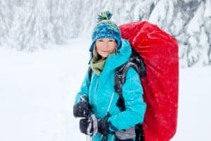 A woman in a light blue jacket with a big red backpack hiking in the winter.