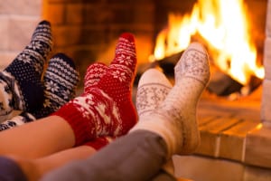 A family of three warming their feet by the fireplace.