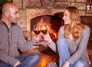 Couple drinking wine in front of the fireplace.