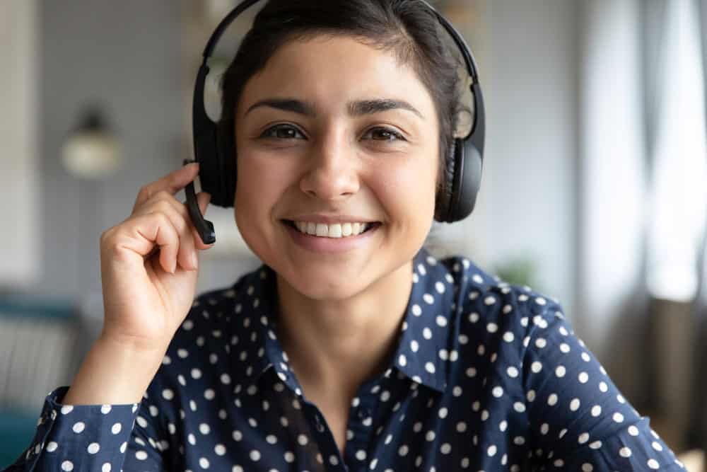 woman smiling at the camera wearing headphones answering customer care questions